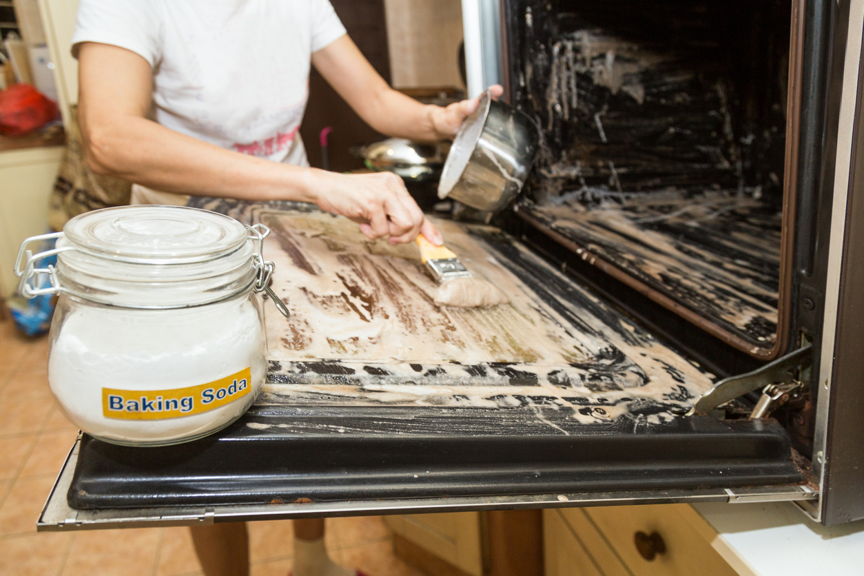 person smearing baking soda paste into their oven for cleaning