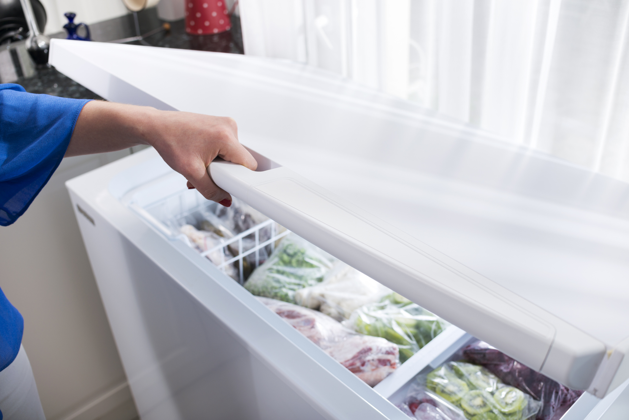 iStock Credit: ilkermetinkursova woman opening the door on her chest freezer