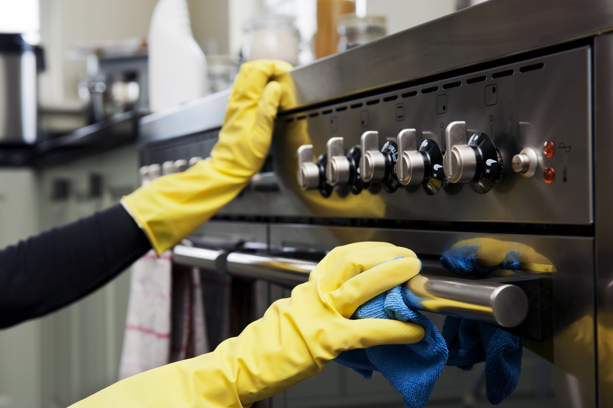 iStock Credit: kirstyokeeffe two hands cleaning a black oven range in a domestic kitchen