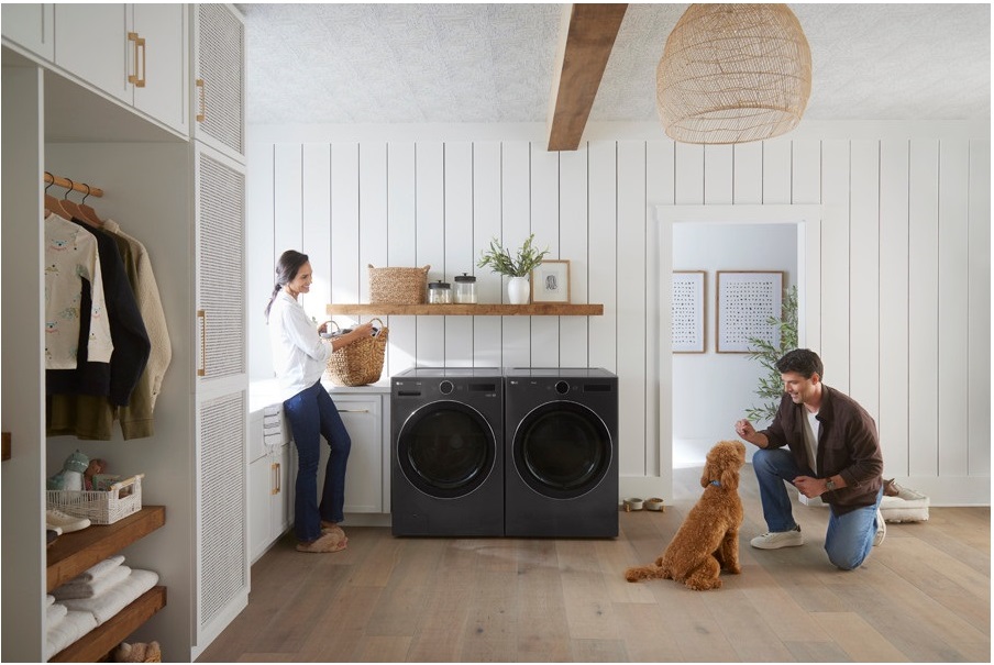 A man, woman, and dog smiling in a laundry room featuring a matching Samsung black washer dryer set