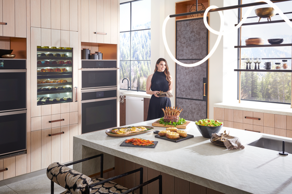 A woman in a black dress in a kitchen featuring Monogram appliances 