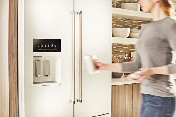 A woman using the water dispenser on a white KitchenAid French door refrigerator 