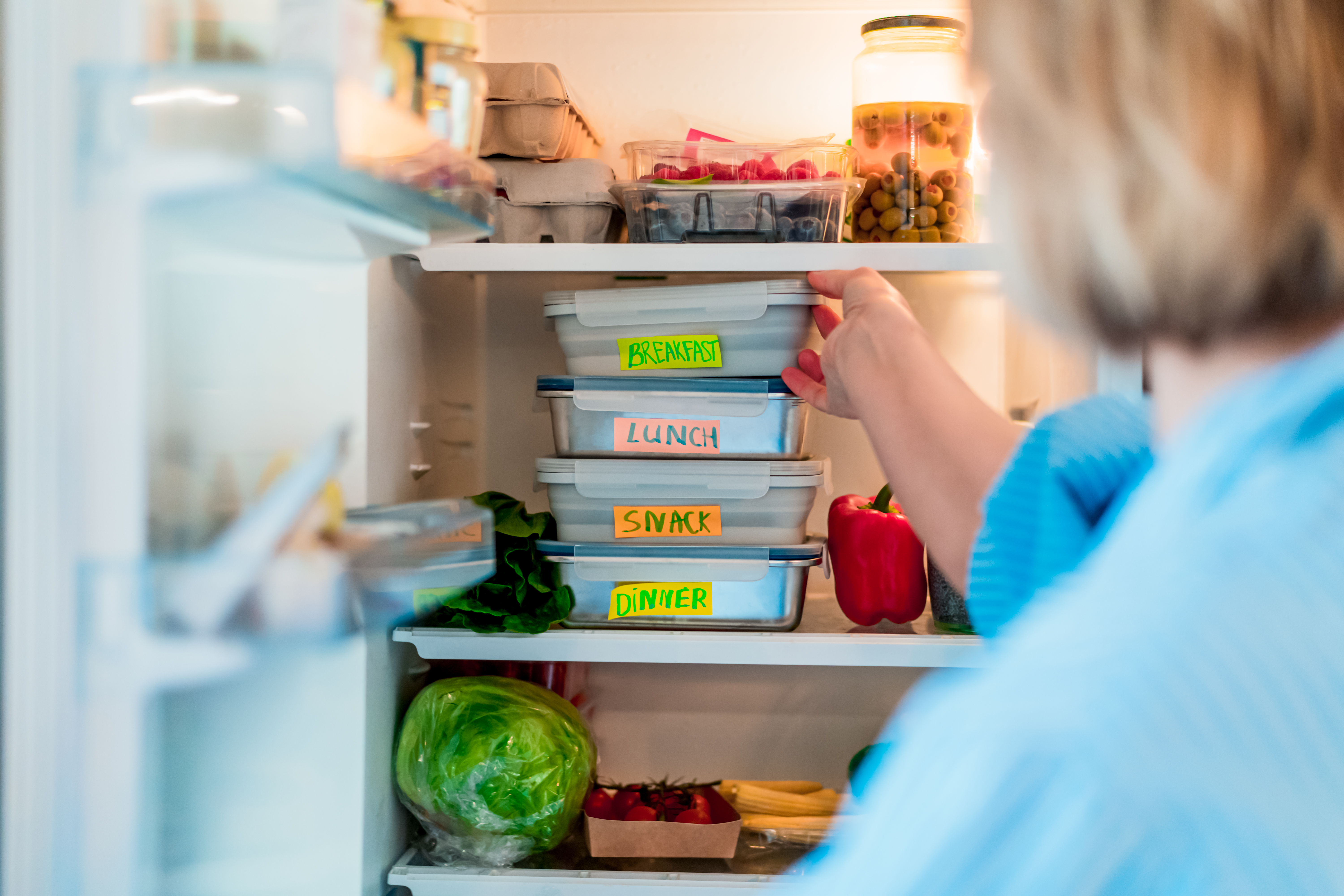 A woman grabbing an item from an overstocked refrigerator 