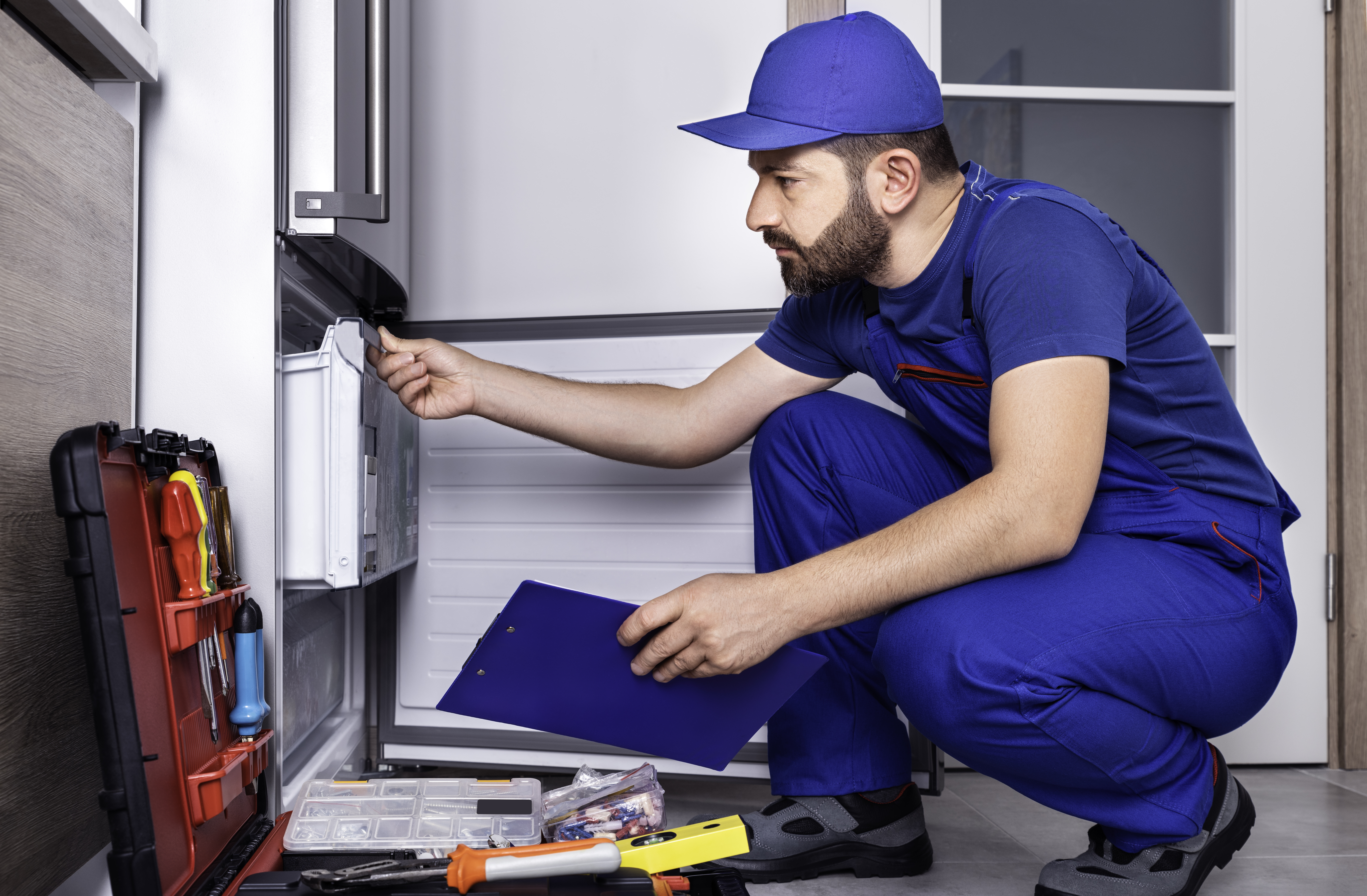 An appliance pro in a blue uniform reviewing a refrigerator 