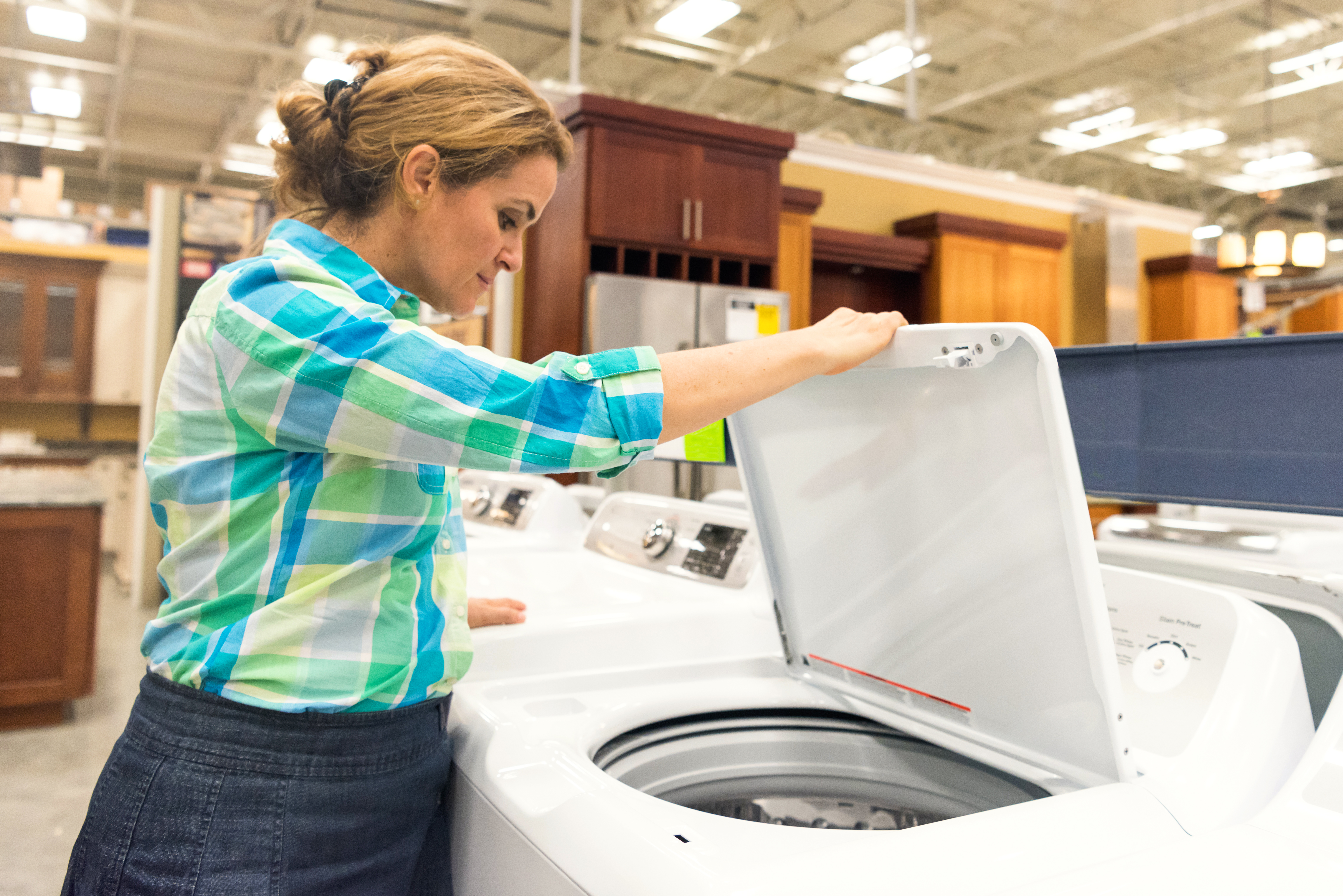 A woman inspecting a top load washing machine in a store