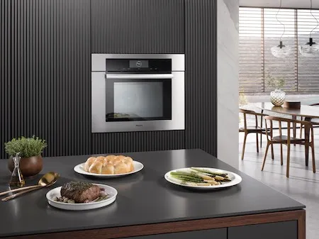 Credit: Miele The Miele DGC 7780 CTS wall oven shown in the background of a kitchen with plates of food in the foreground