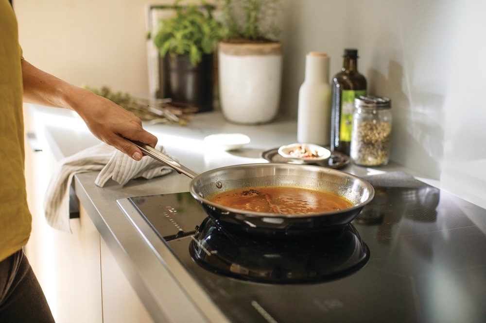 closeup of home cook using an Electrolux induction cooktop to reduce sauce in a pan