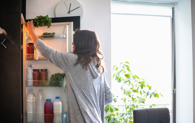 Front view of a woman reaching into her freezerless refrigerator Front view of a woman reaching into her freezerless refrigerator