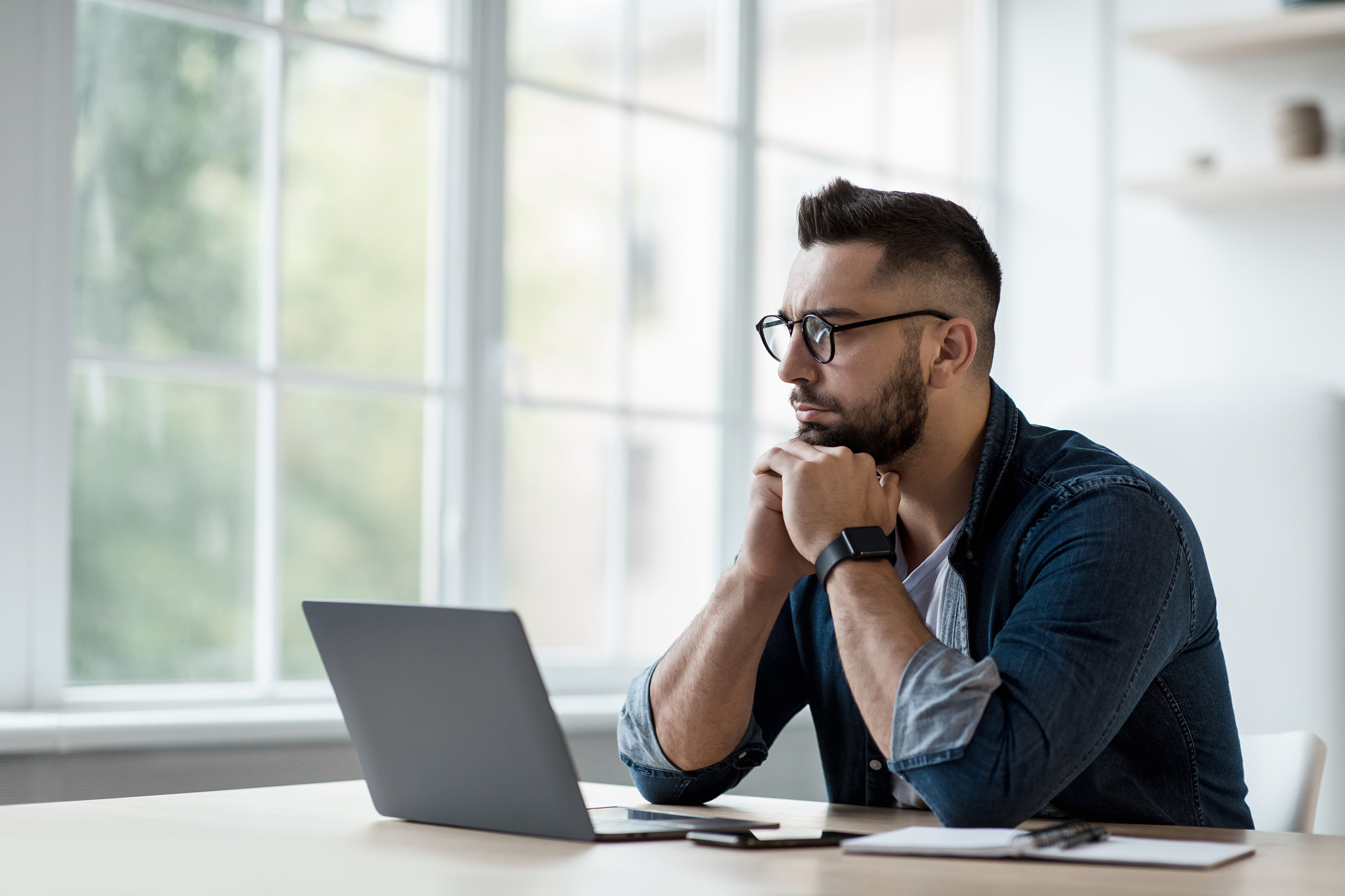 A young man sitting and thinking while using a laptop 