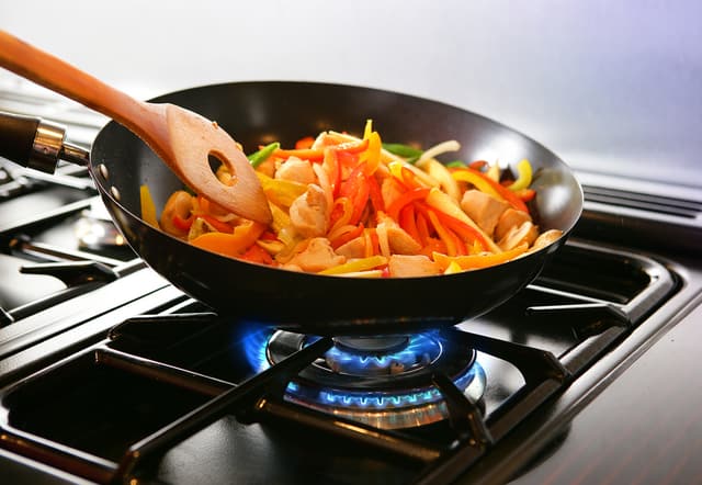 Close view of someone using a wok to cook vegetables on a gas stove Close view of someone using a wok to cook vegetables on a gas stove
