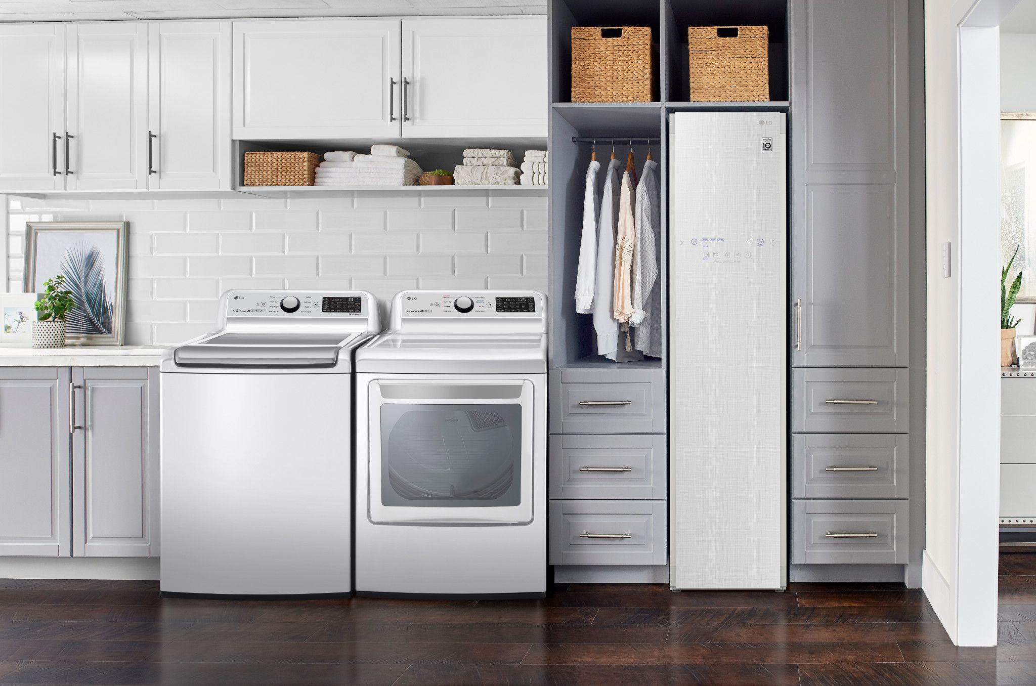 White LG top load washer and dryer in a laundry room with dark wood floors and gray cabinets