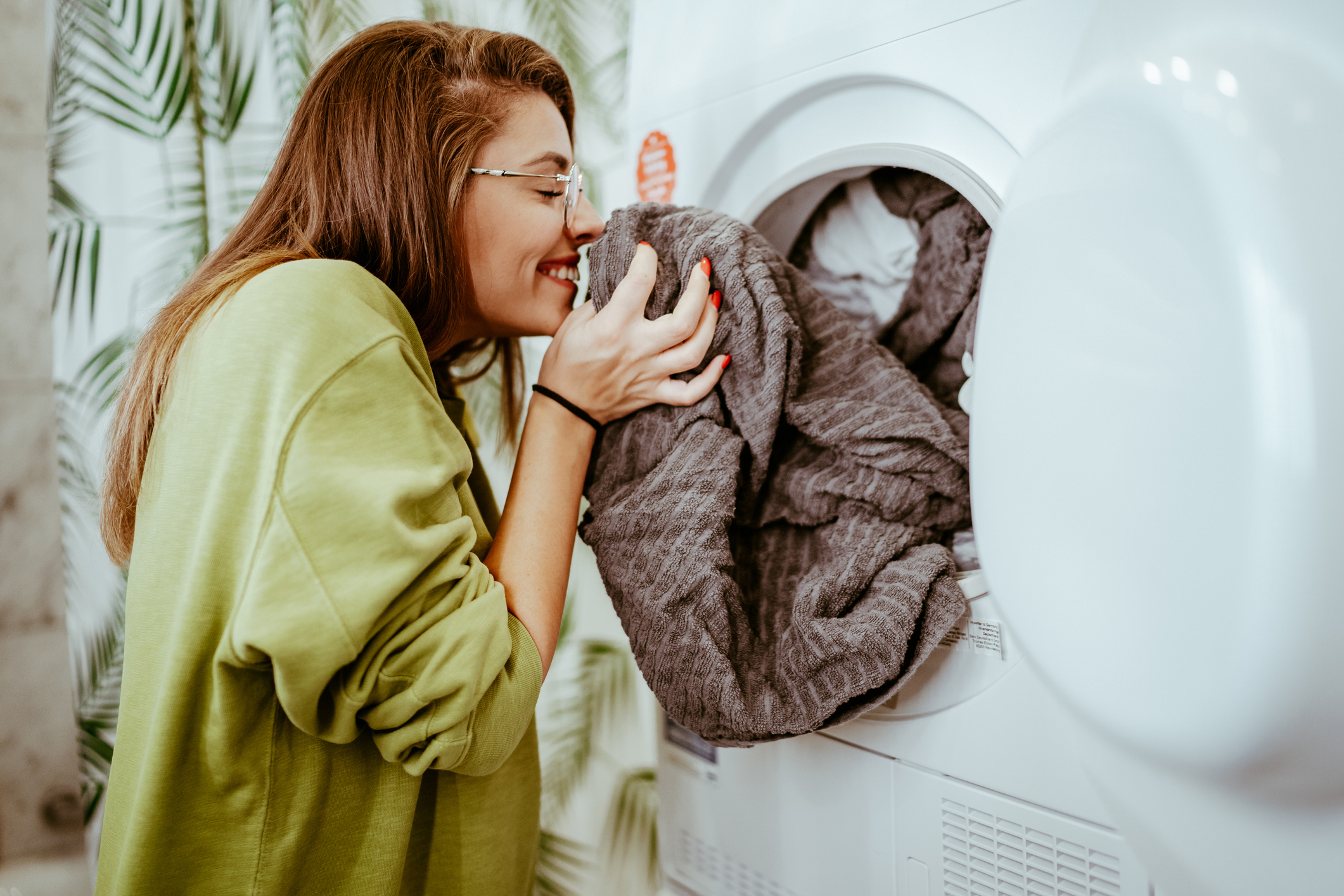 iStock Credit: bojanstory young woman smells freshly dried towel as she unloads her clothes dryer
