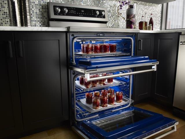 View of an opened electric oven with cheesecake cups cooking inside View of an opened electric oven with cheesecake cups cooking inside
