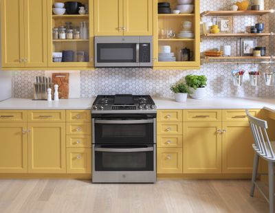 A GE double oven range and and microwave in a yellow-themed kitchen