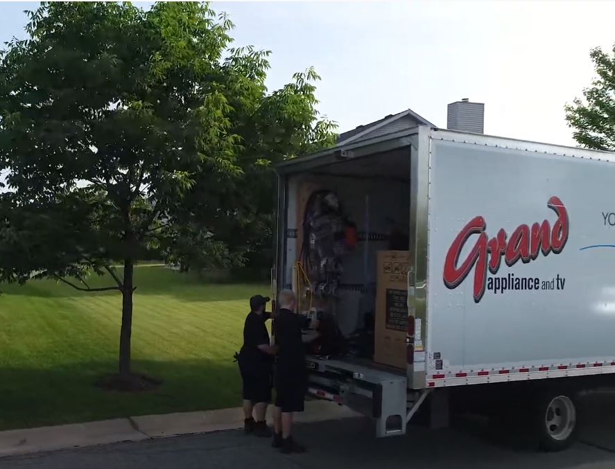 Two Grand Appliance installation pros preparing to move a fridge out of the delivery truck and into a home