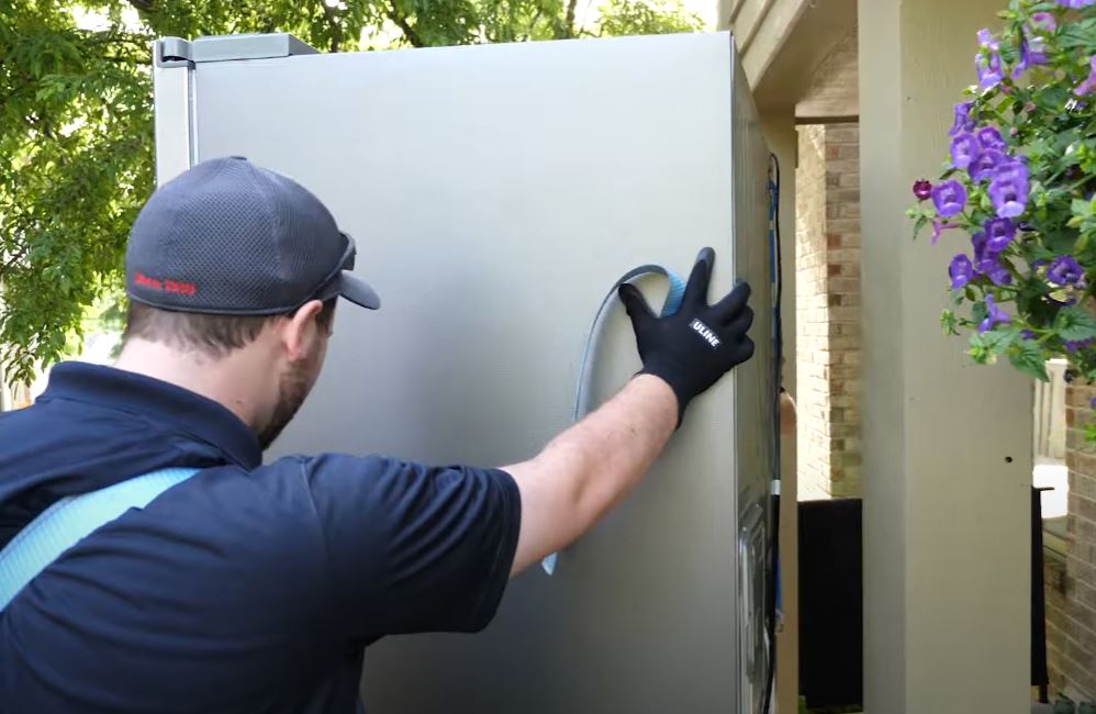 Grand Appliance installation pro sliding a fridge through a front door
