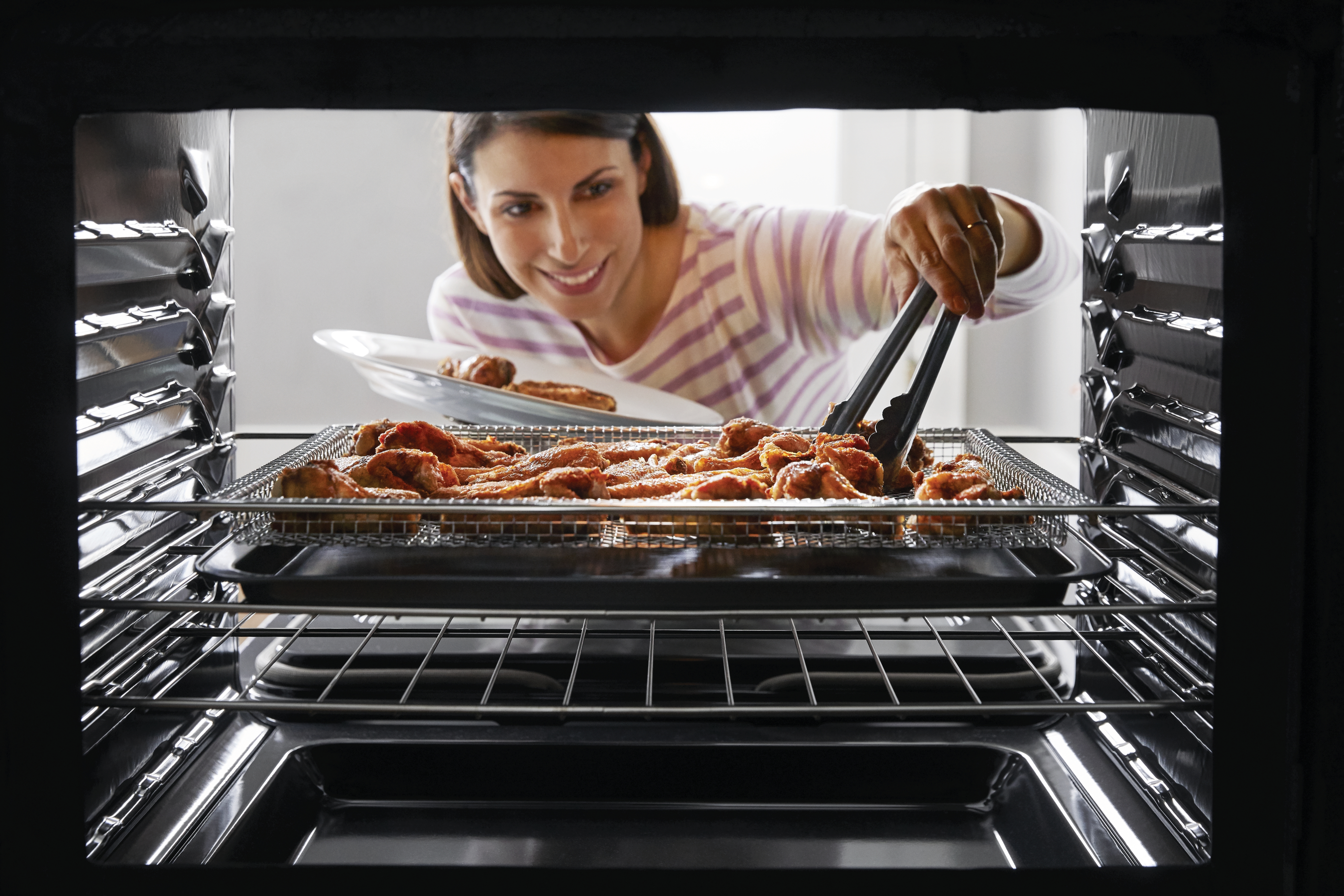 Credit: Frigidaire Gallery Woman retrieving a tray of chicken wings from inside a Frigidaire Gallery Air Fry oven