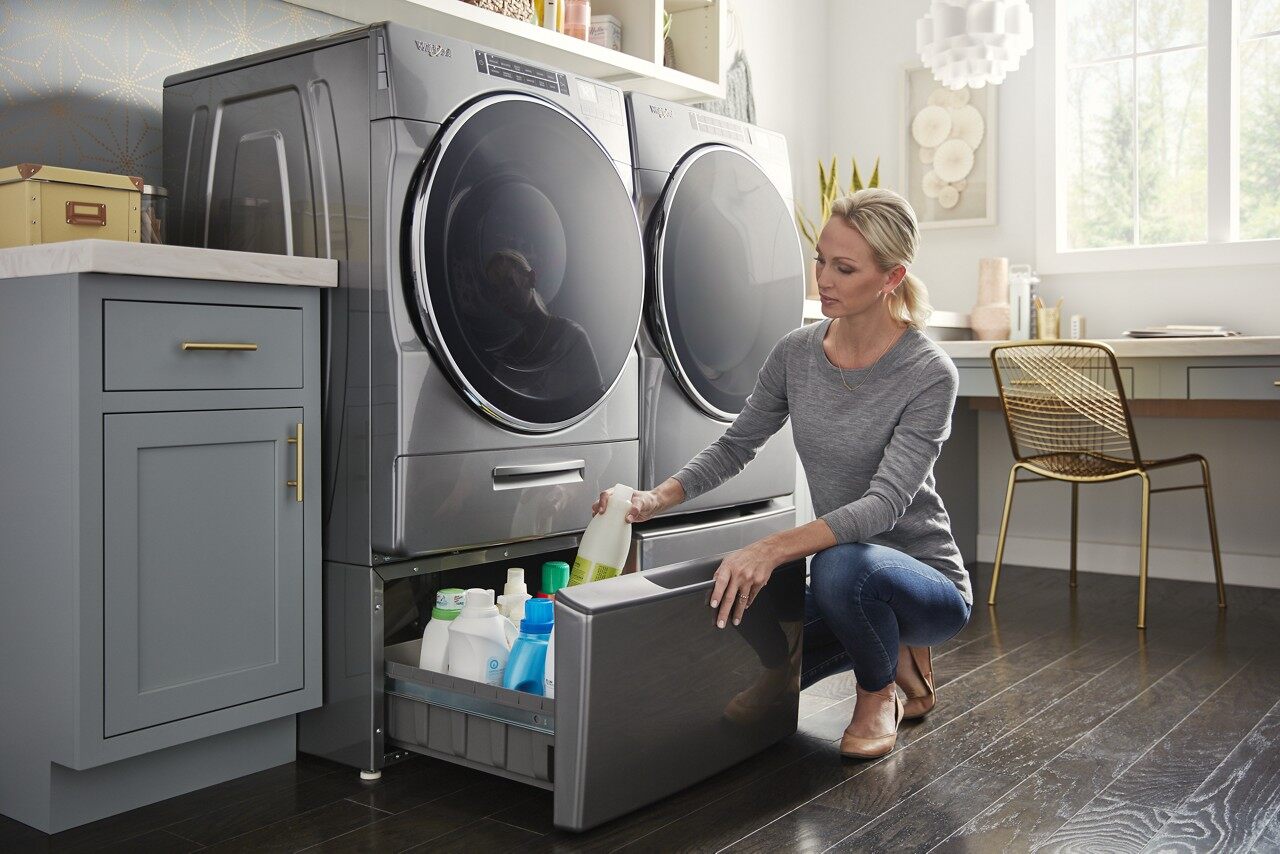 A woman storing detergent in the pedestal of a Whirlpool front load washer and dryer set 