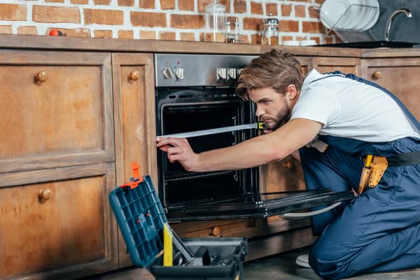 An appliance technician measuring an oven - iStock Credit: LightFieldStudios