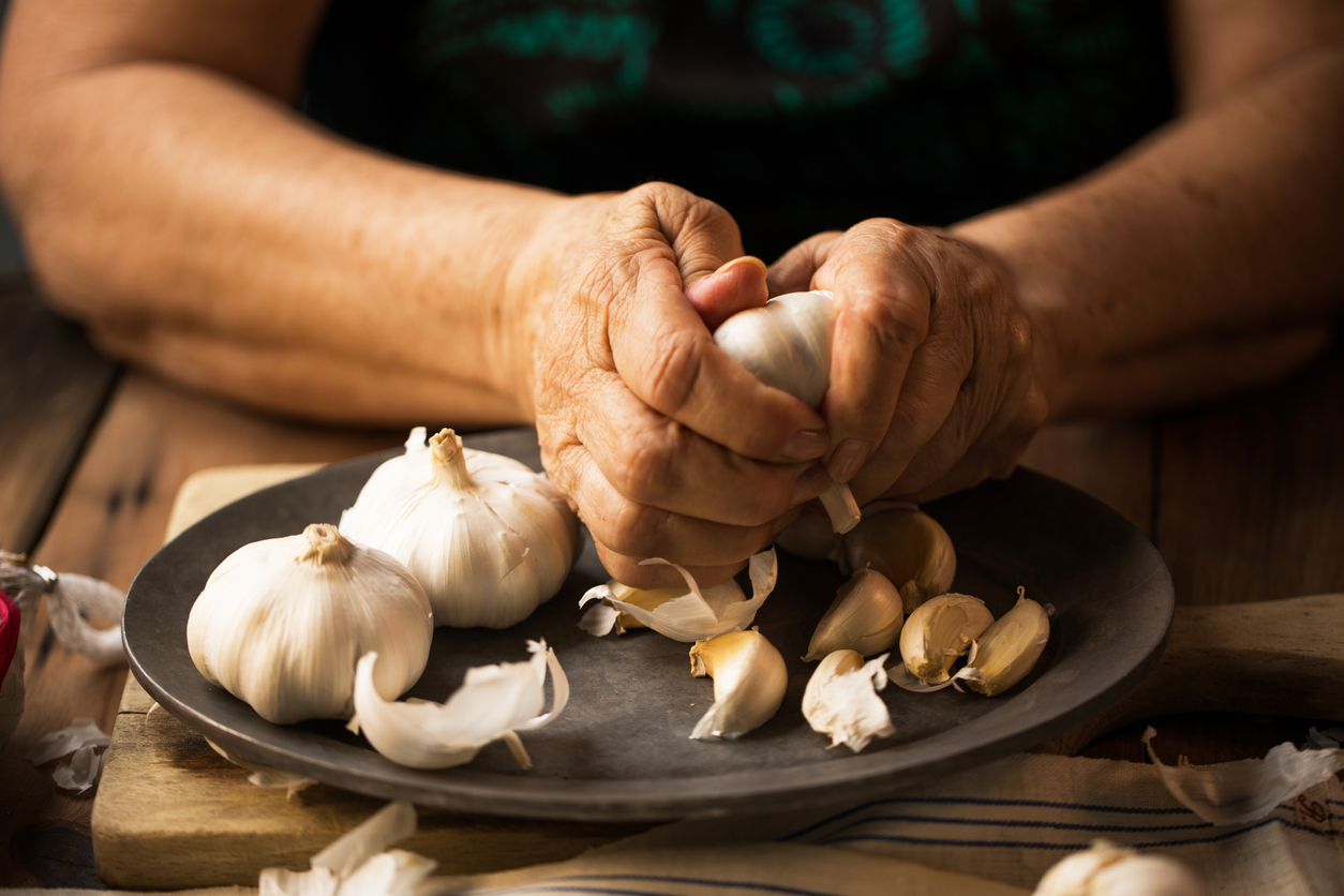 iStock Credit: THEPALMER close-up of a woman’s hands removing garlic skin over a plate