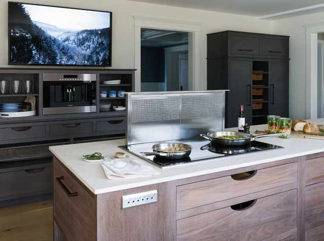 Front view of a modern kitchen with a downdraft range hood behind a cooktop in the island