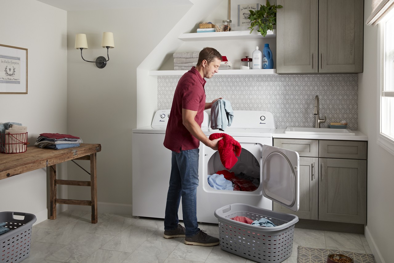 A man in a red shirt taking clothes out of an Amana washer and dryer set 