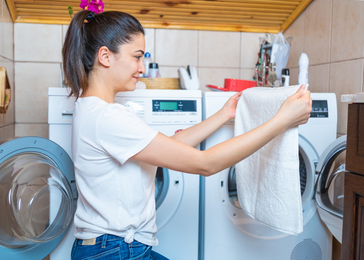 iStock Credit: aquaArts studio woman smiles as she takes clothes out of front-loading washer
