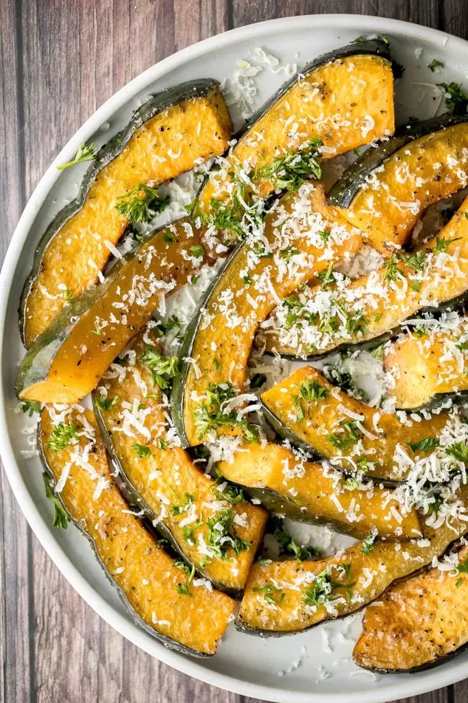 Credit Source: Ahead of Thyme Overhead shot of acorn squash in crescent slices dusted with parmesan cheese