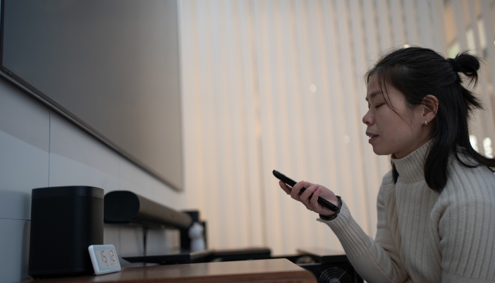 A woman turning on the TV with a soundbar and satellite speakers hooked up