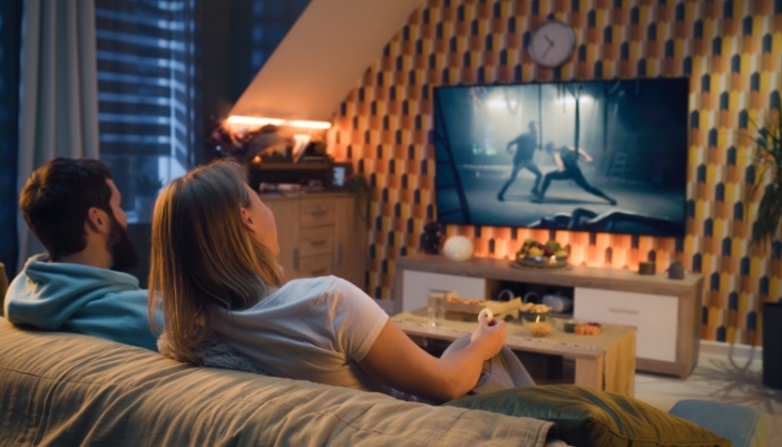 A couple watching TV in a well-lit room with ambient lighting