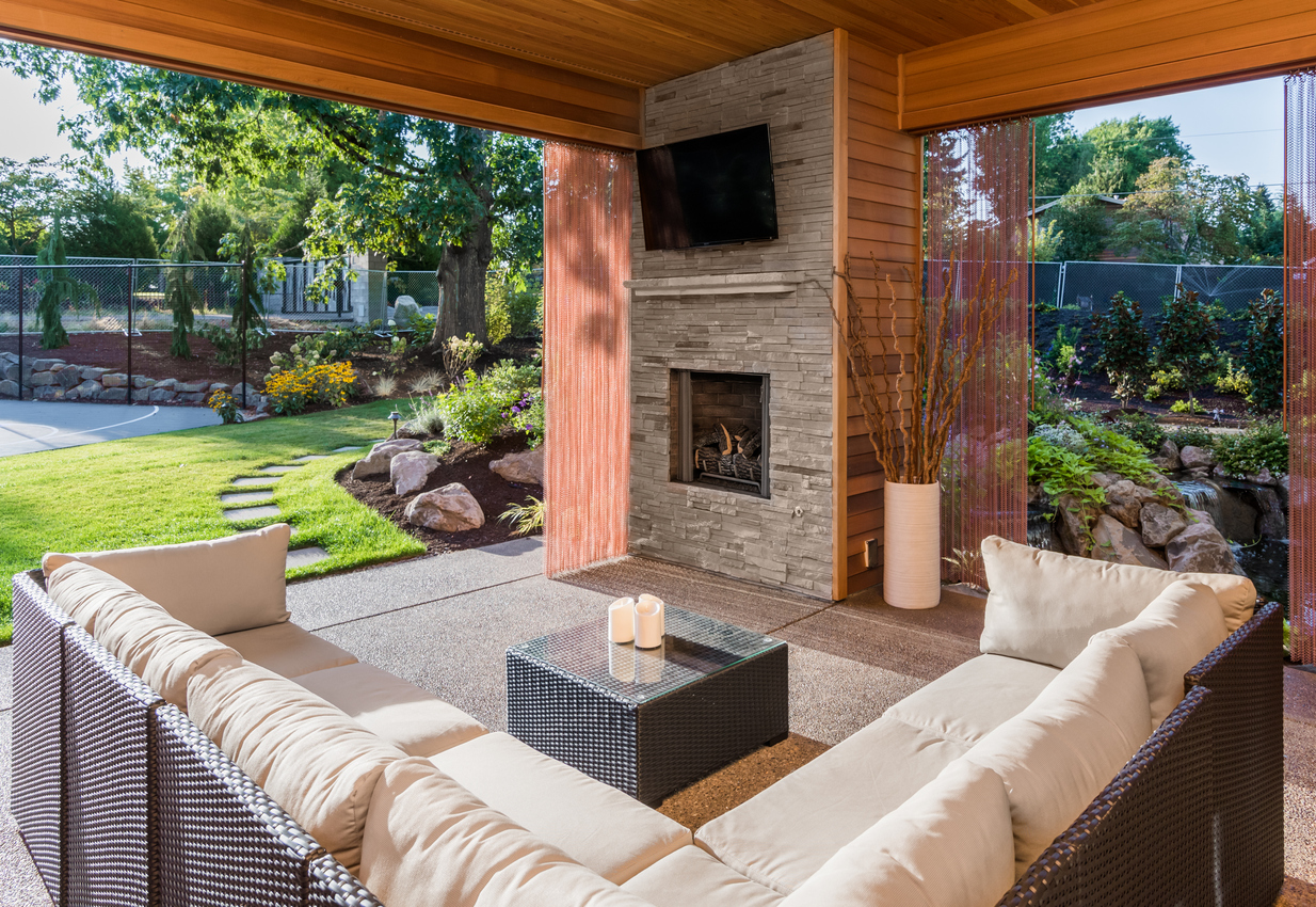 iStock Credit: hikesterson covered patio with fireplace, tv, and couch, with view of lush green grass and landscaping