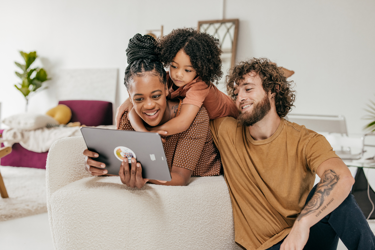 iStock Credit: kate_sept2004 family of three sitting on their living room sofa with tablet
