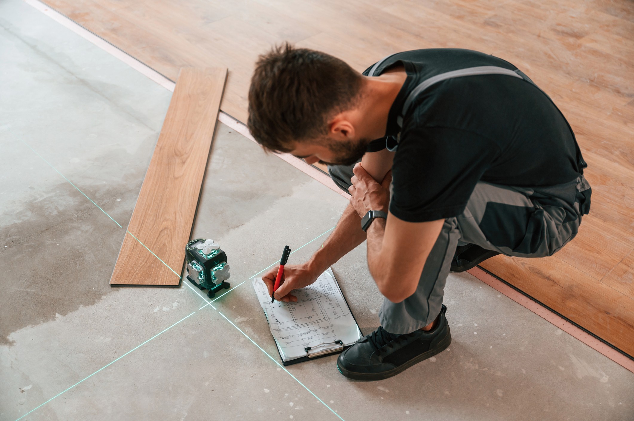 A flooring installer using a laser to take down calculations