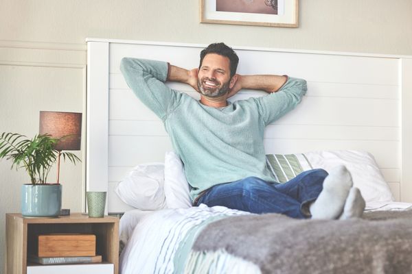iStock Credit: DMP A smiling man in a teal shirt sitting up against a white headboard