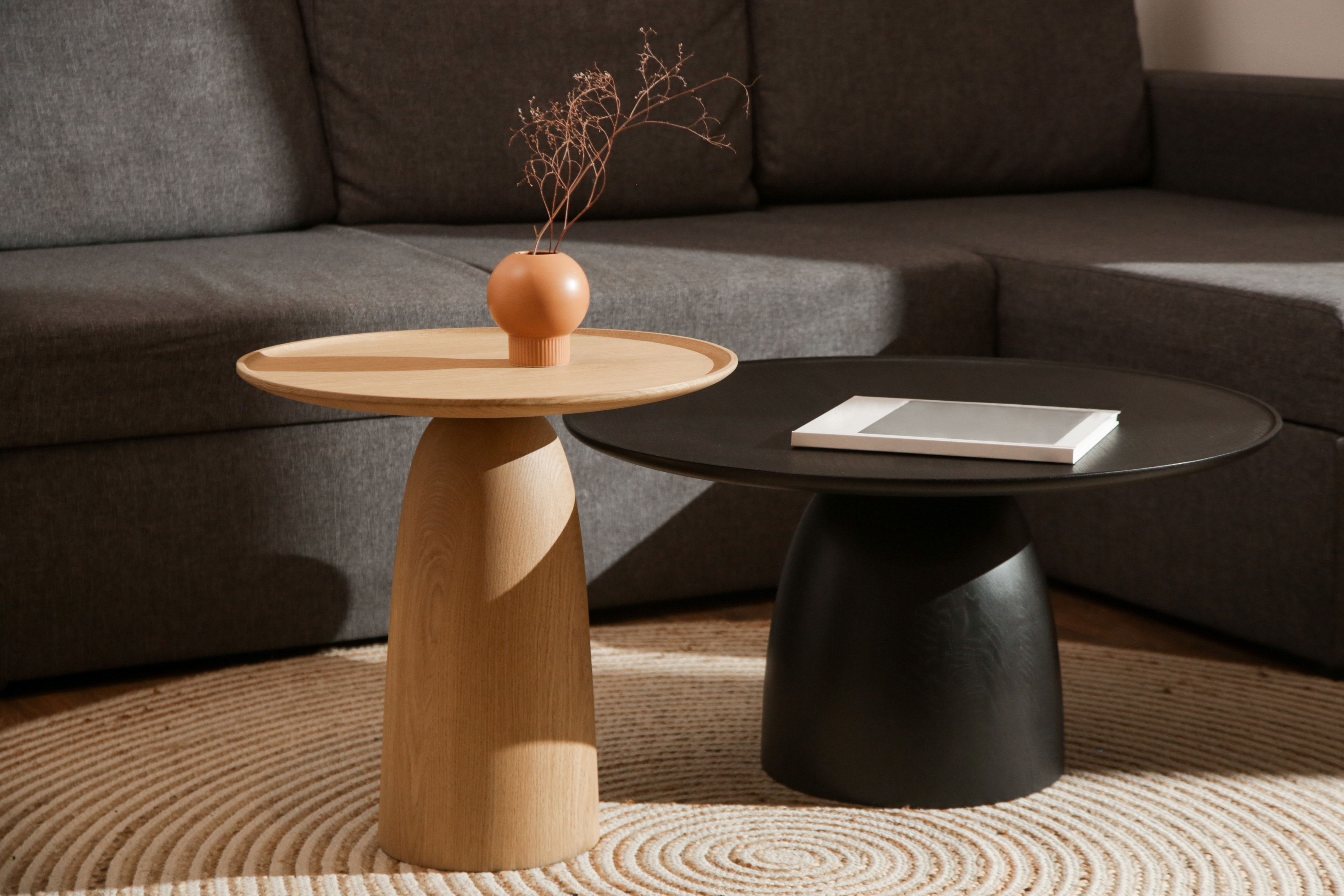 A modern black and wooden round pedestal coffee table and end table with decor