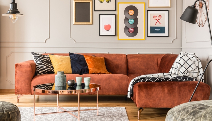 A rust colored L-shaped couch is surrounded by retro inspired home decor. 