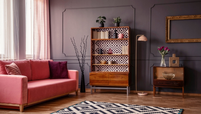 A black and white patterned bookcase next to a mauve couch.