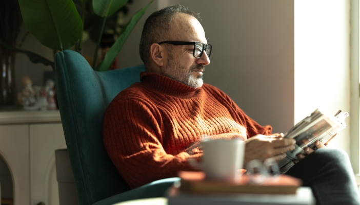 An older gentleman sitting in a chair reading at home.