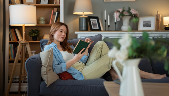 A woman sits in a chair at home and reads her book.