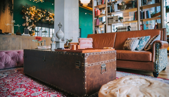 An antique trunk sits in the forefront of a modern living room with a full bookcase in back.