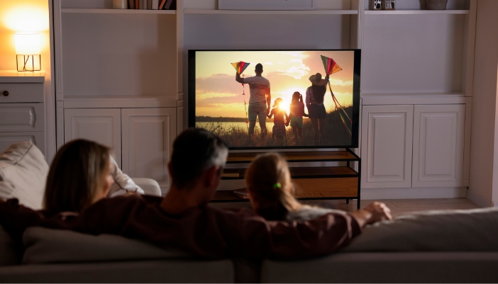 An over the shoulder look at a family watching a movie at home.