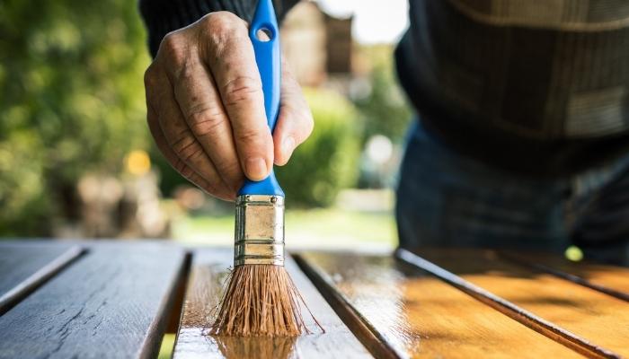 Furn_Protect-Outdoor-Furniture_4.jpg Man adding coat of sealant to wood furniture