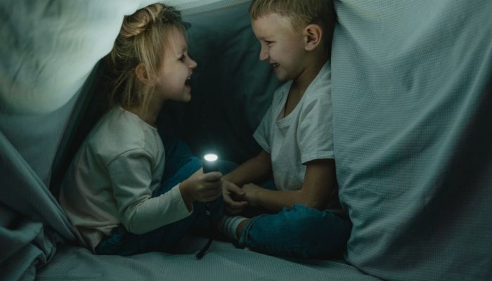 Furn_Summer-Kids-Activities_2.jpg Two kids under a blanket fort with a flashlight