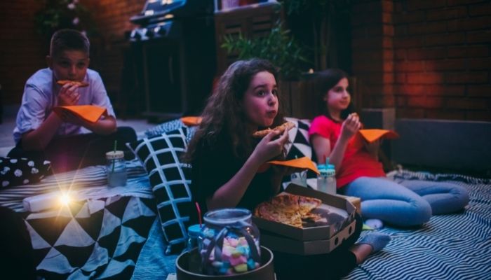 Furn_Summer-Kids-Activities_4.jpg Three kids eating pizza and watching a movie outside
