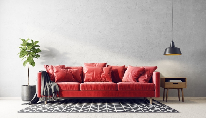 A red velvet couch rests on a black and white rug and in front of a gray wall.
