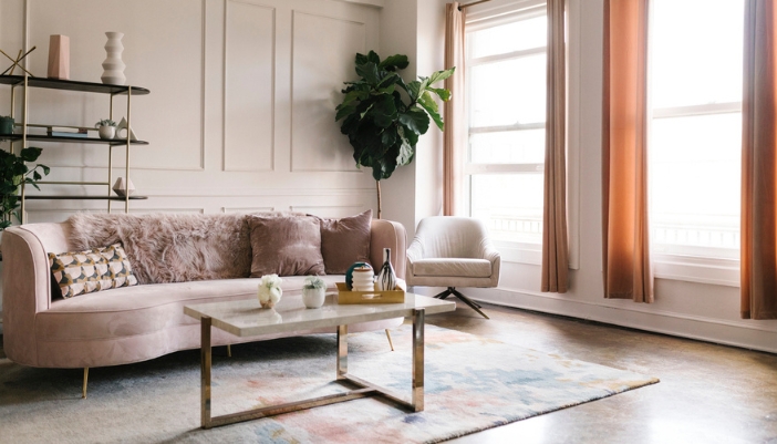 A light pink curved couch in a retro inspired, brightly lit living room.