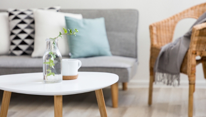 Close-up of a white round coffee table with a gray couch and natural wooden furniture behind.