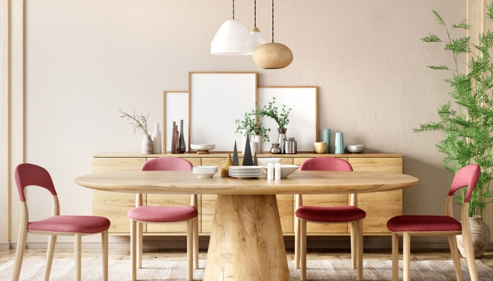 A dining room with warm, wooden tones and a round dining table and simple red upholstered chairs.