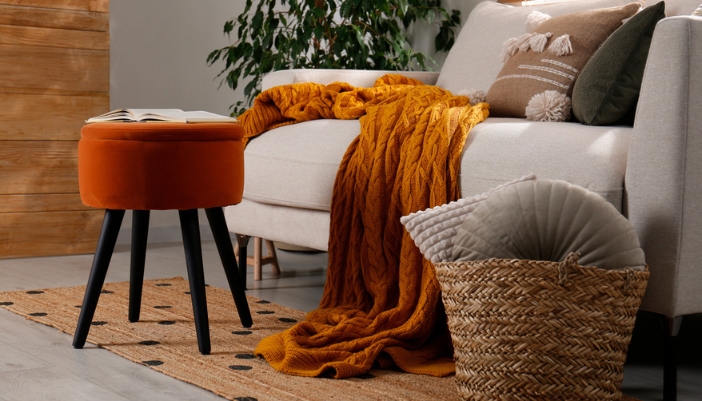 An oversized armchair with textured pillows and a thick, rust colored blanket ready to curl up in.