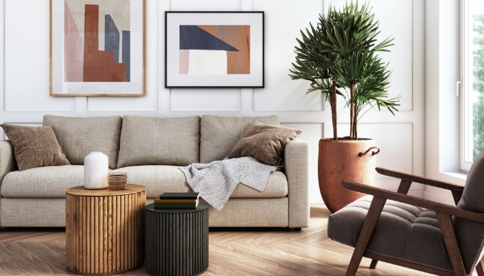A tan couch sit sin a neutral living room with geometric designs behind it.